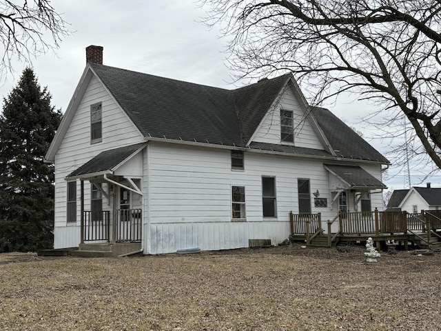 rear view of house with a shingled roof, a chimney, and a deck