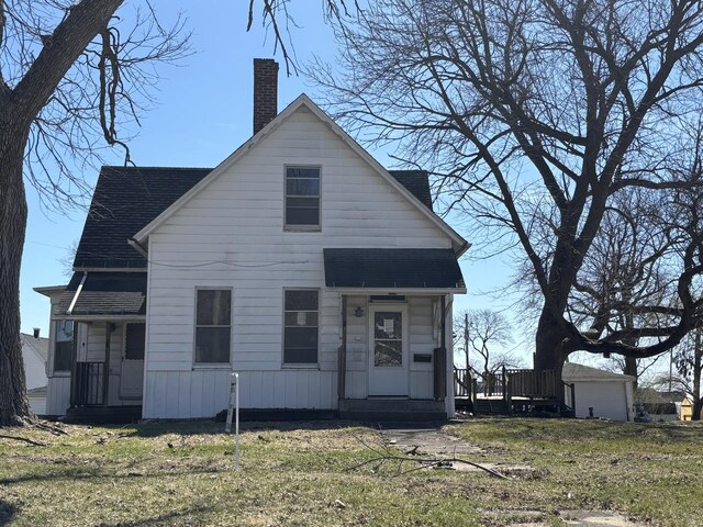 view of front facade featuring a front lawn, a chimney, and a shingled roof