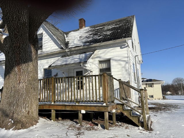 snow covered back of property with a chimney and a wooden deck