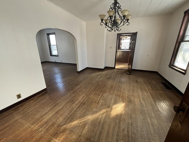 unfurnished dining area featuring plenty of natural light, arched walkways, and dark wood-type flooring