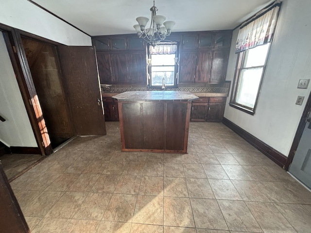 kitchen featuring tile countertops, dark brown cabinetry, baseboards, backsplash, and a center island