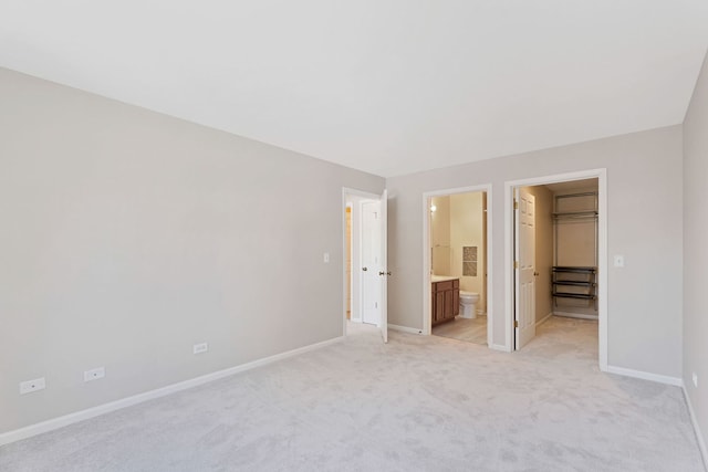 unfurnished bedroom featuring ensuite bathroom, a walk in closet, light carpet, and a closet