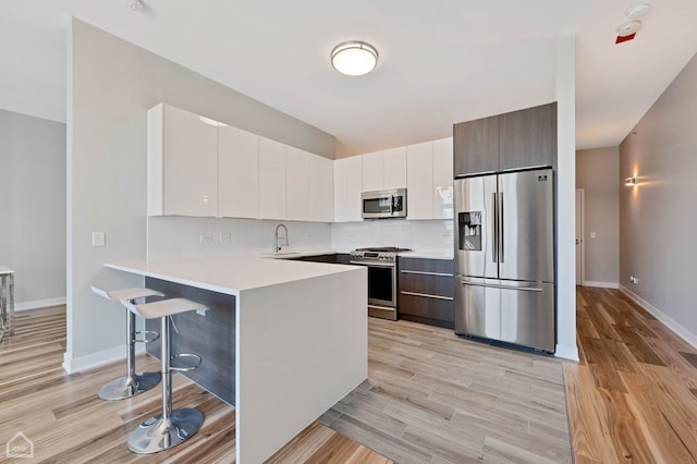 kitchen featuring a breakfast bar, sink, white cabinetry, kitchen peninsula, and stainless steel appliances