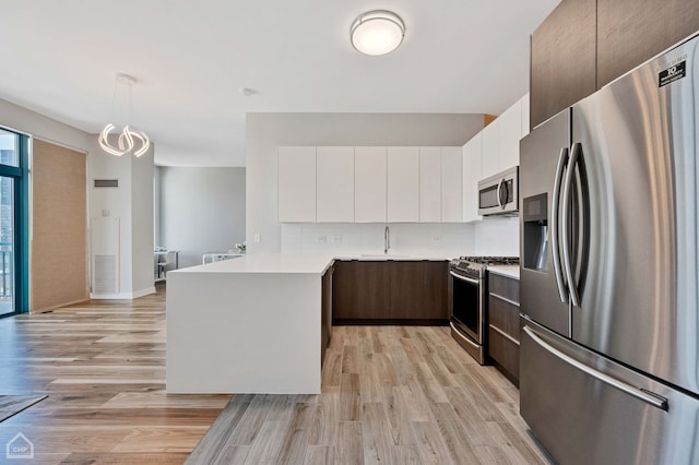 kitchen featuring hanging light fixtures, white cabinetry, appliances with stainless steel finishes, and light hardwood / wood-style floors