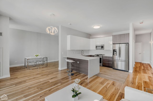 kitchen featuring sink, a breakfast bar area, light hardwood / wood-style flooring, appliances with stainless steel finishes, and pendant lighting