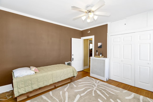 bedroom featuring crown molding, ceiling fan, wood-type flooring, and a closet