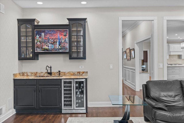 bar featuring dark wood-type flooring, sink, light stone counters, beverage cooler, and backsplash