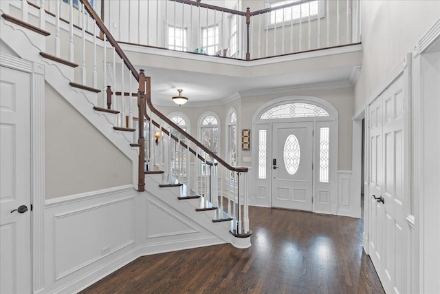 foyer entrance featuring crown molding, dark wood-type flooring, a healthy amount of sunlight, and a towering ceiling