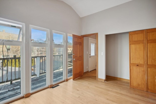 doorway to outside with high vaulted ceiling and light hardwood / wood-style floors