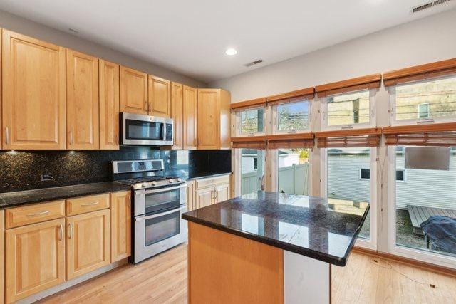 kitchen featuring light hardwood / wood-style flooring, stainless steel appliances, a center island, and dark stone counters