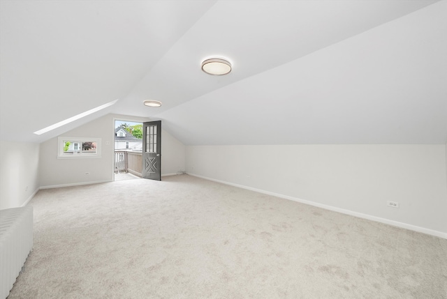 additional living space featuring radiator heating unit, baseboards, light carpet, and vaulted ceiling