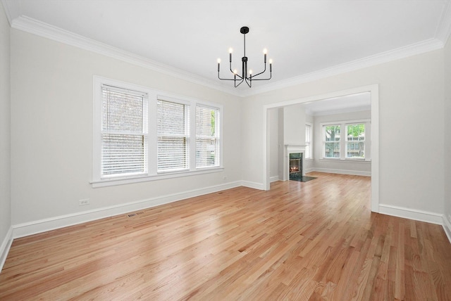 unfurnished living room with a chandelier, light wood-type flooring, ornamental molding, baseboards, and a fireplace with flush hearth