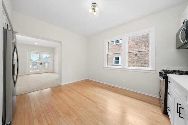 unfurnished dining area with light wood finished floors, baseboards, and french doors