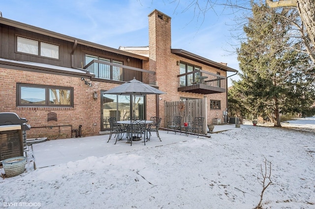 snow covered back of property featuring a balcony and central air condition unit