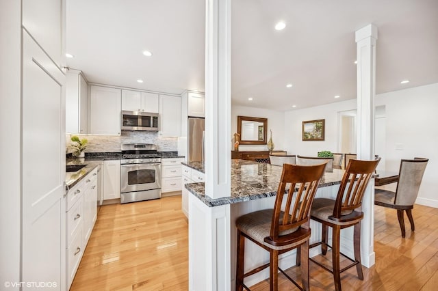 kitchen with white cabinetry, stainless steel appliances, a breakfast bar, and ornate columns