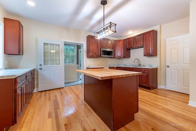 kitchen with pendant lighting, sink, a kitchen island, wood counters, and light wood-type flooring