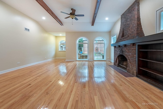 unfurnished living room featuring ceiling fan, a fireplace, beamed ceiling, and light wood-type flooring