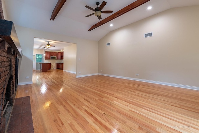 unfurnished living room featuring beamed ceiling, ceiling fan, a brick fireplace, and light wood-type flooring