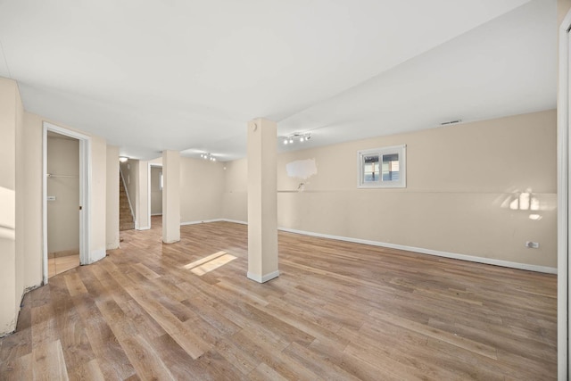 basement with rail lighting and light hardwood / wood-style floors