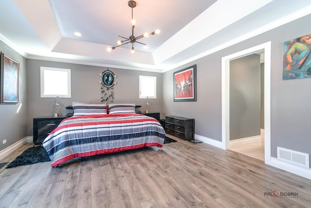 bedroom with light hardwood / wood-style flooring, a chandelier, a raised ceiling, and crown molding