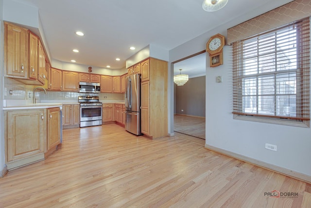 kitchen featuring pendant lighting, sink, light hardwood / wood-style flooring, appliances with stainless steel finishes, and backsplash