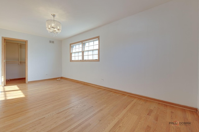 spare room featuring a chandelier and light wood-type flooring