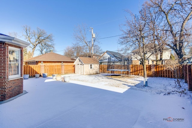 snowy yard featuring a storage unit and a trampoline