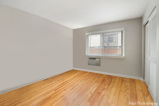 unfurnished bedroom with a wall mounted air conditioner, light hardwood / wood-style floors, and a closet