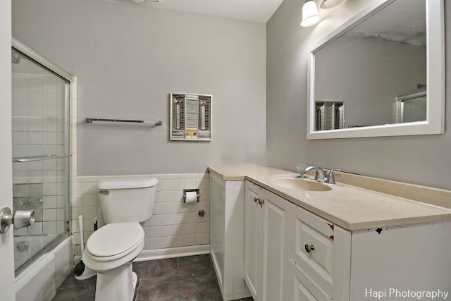 full bathroom featuring combined bath / shower with glass door, tile walls, tile patterned flooring, vanity, and toilet