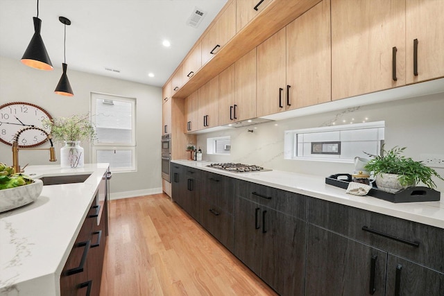 kitchen featuring pendant lighting, stainless steel gas stovetop, light brown cabinetry, light stone countertops, and light hardwood / wood-style floors