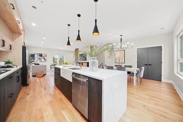 kitchen with dark brown cabinets, light hardwood / wood-style flooring, appliances with stainless steel finishes, decorative light fixtures, and a center island with sink