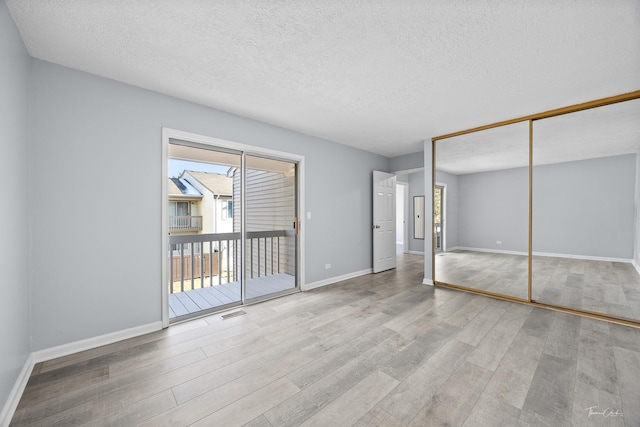 unfurnished bedroom with a textured ceiling, access to exterior, light hardwood / wood-style floors, and a closet