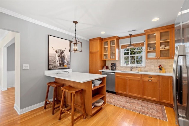 kitchen featuring sink, stainless steel appliances, a kitchen bar, decorative light fixtures, and light wood-type flooring