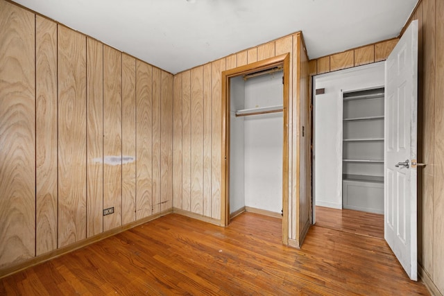 unfurnished bedroom with hardwood / wood-style flooring, a closet, and wooden walls