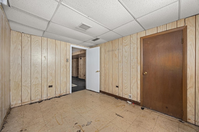 spare room featuring a paneled ceiling and wood walls