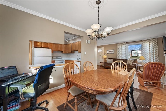 dining room with rail lighting, sink, ornamental molding, a notable chandelier, and light wood-type flooring