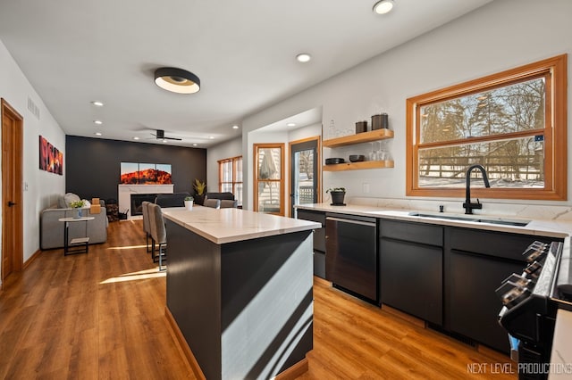 kitchen with sink, light hardwood / wood-style flooring, ceiling fan, a center island, and black dishwasher