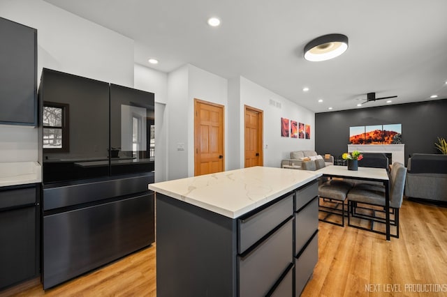 kitchen with light stone counters, gray cabinetry, a kitchen island, and light hardwood / wood-style flooring