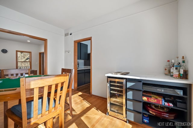 dining space with bar, beverage cooler, and light wood-type flooring