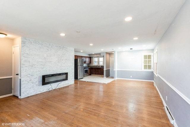 unfurnished living room with sink, a stone fireplace, baseboard heating, and light wood-type flooring