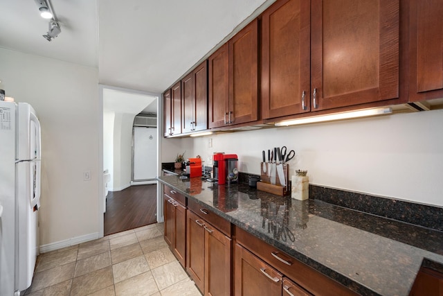 kitchen featuring light tile patterned floors, dark stone counters, rail lighting, and white fridge