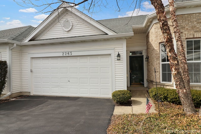 view of front facade with an attached garage, brick siding, driveway, and roof with shingles