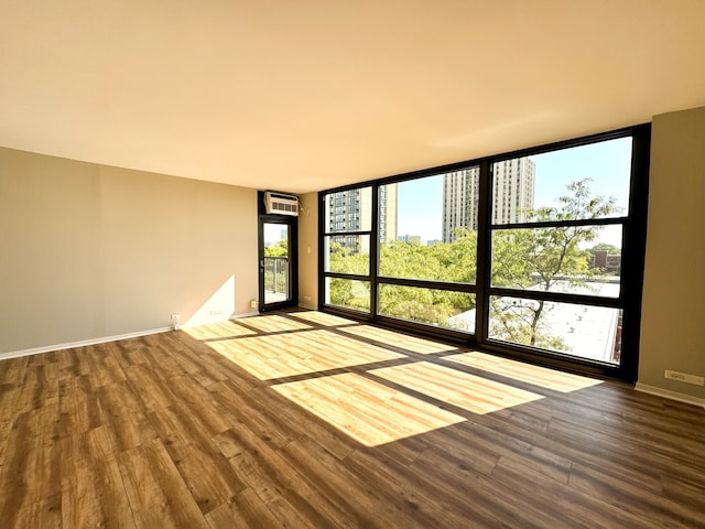 empty room featuring a wall mounted air conditioner, a wealth of natural light, a wall of windows, and wood-type flooring