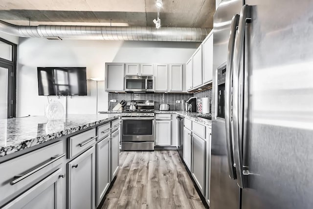 kitchen featuring gray cabinetry, light stone counters, light wood-type flooring, stainless steel appliances, and decorative backsplash