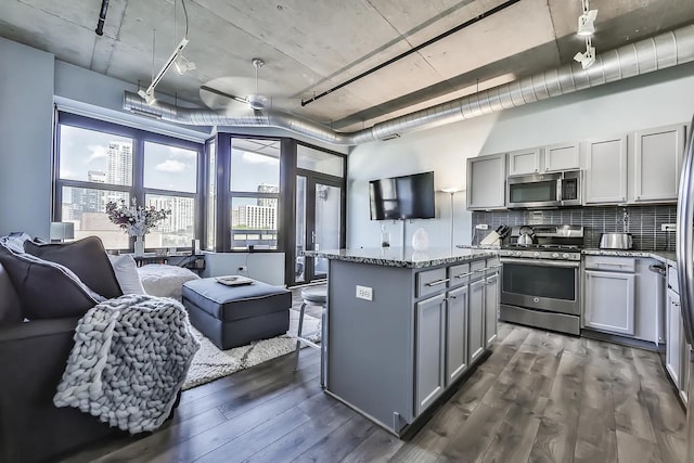 kitchen with dark wood-type flooring, stainless steel appliances, dark stone counters, and gray cabinetry