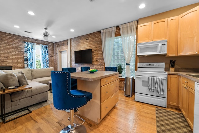 kitchen with brick wall, white appliances, a center island, light hardwood / wood-style floors, and light brown cabinetry