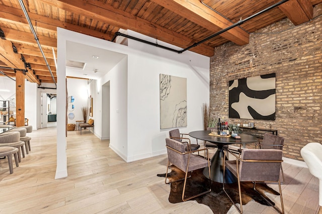 dining area with beamed ceiling, brick wall, light hardwood / wood-style flooring, and wooden ceiling