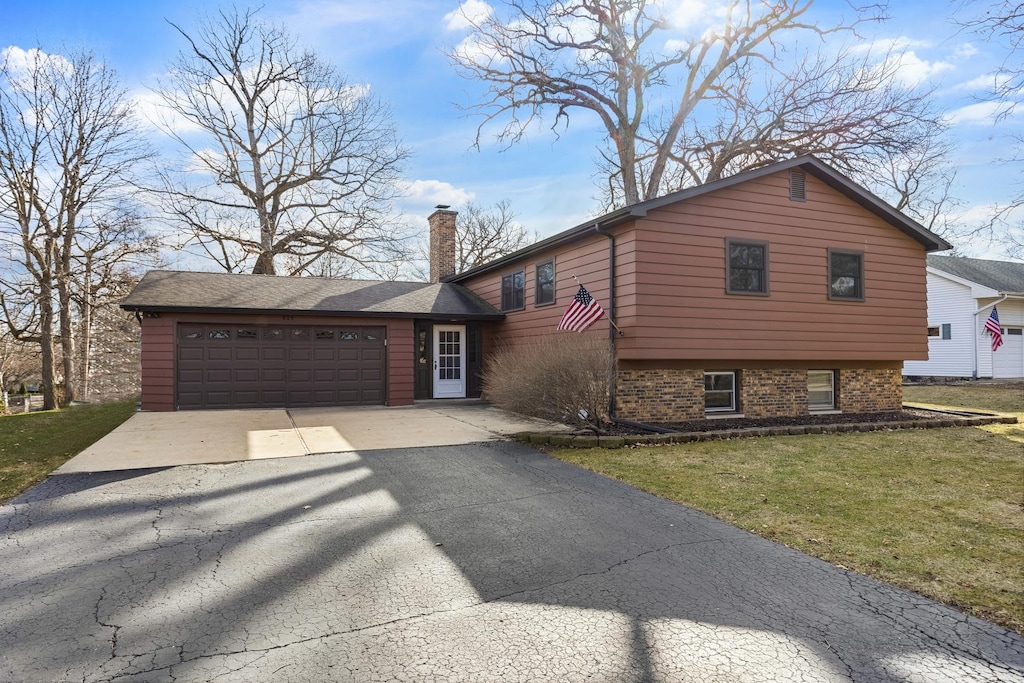 tri-level home with a garage, a front yard, driveway, and a chimney