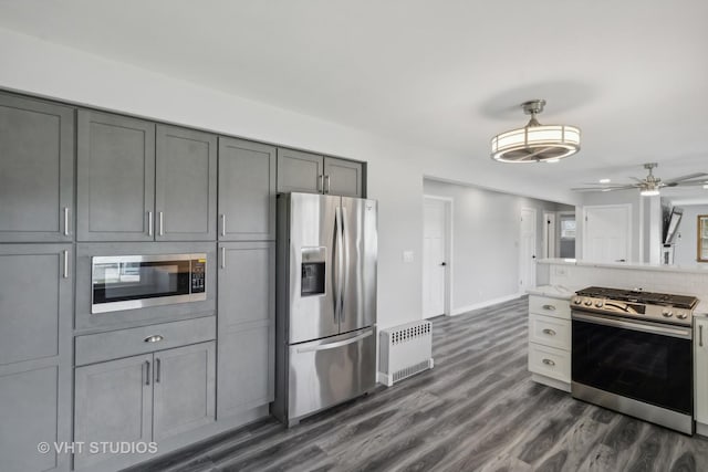 kitchen featuring radiator heating unit, appliances with stainless steel finishes, dark wood-type flooring, tasteful backsplash, and gray cabinets