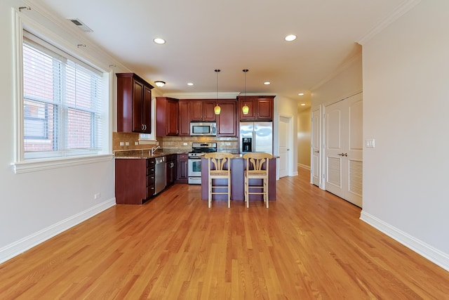 kitchen featuring appliances with stainless steel finishes, a breakfast bar, pendant lighting, a center island, and light stone counters